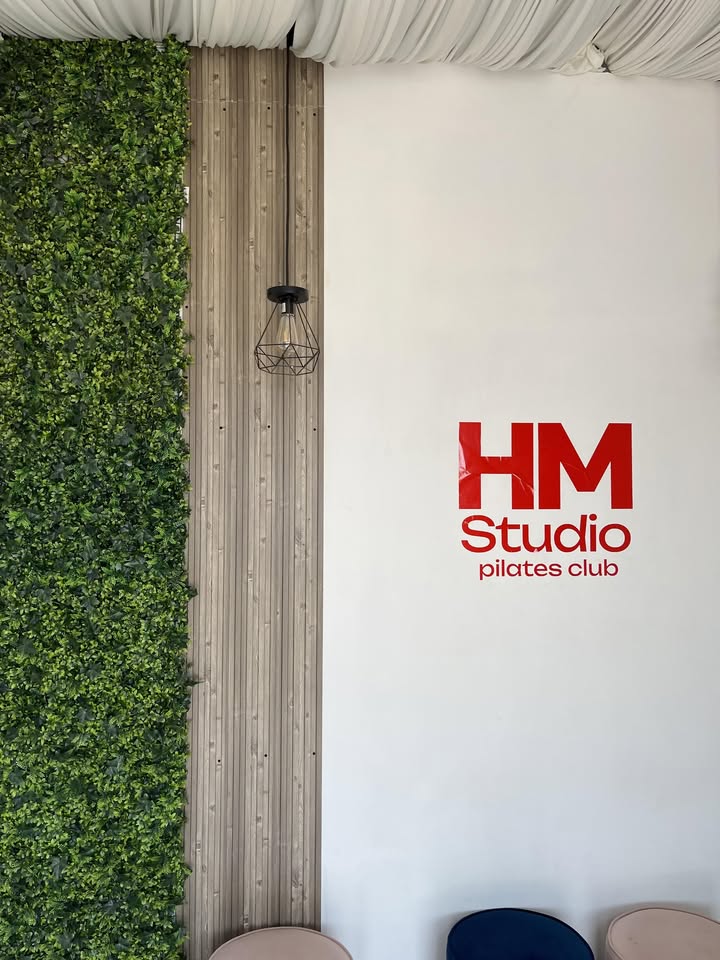 Interior del estudio HM Studio Pilates Club con muro verde y el logotipo en la pared